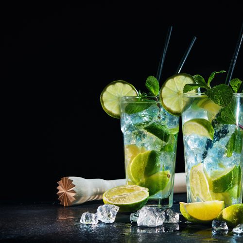 Two glasses of mojito cocktail with fresh lime and mint on a black stone board